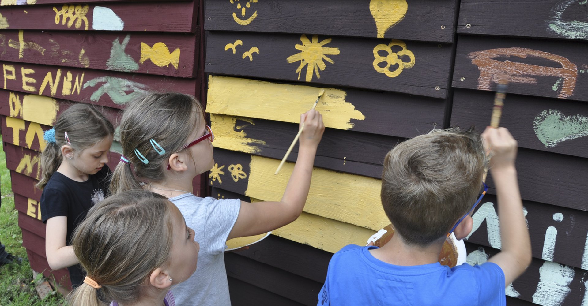 Kinder bemalen eine Holzhütte mit Rötelfarben